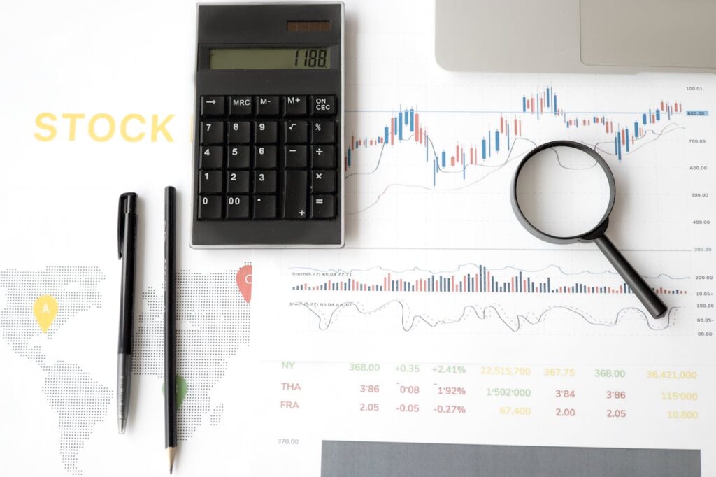 Flat lay of stock market analysis tools including calculator, graphs, and magnifying glass.