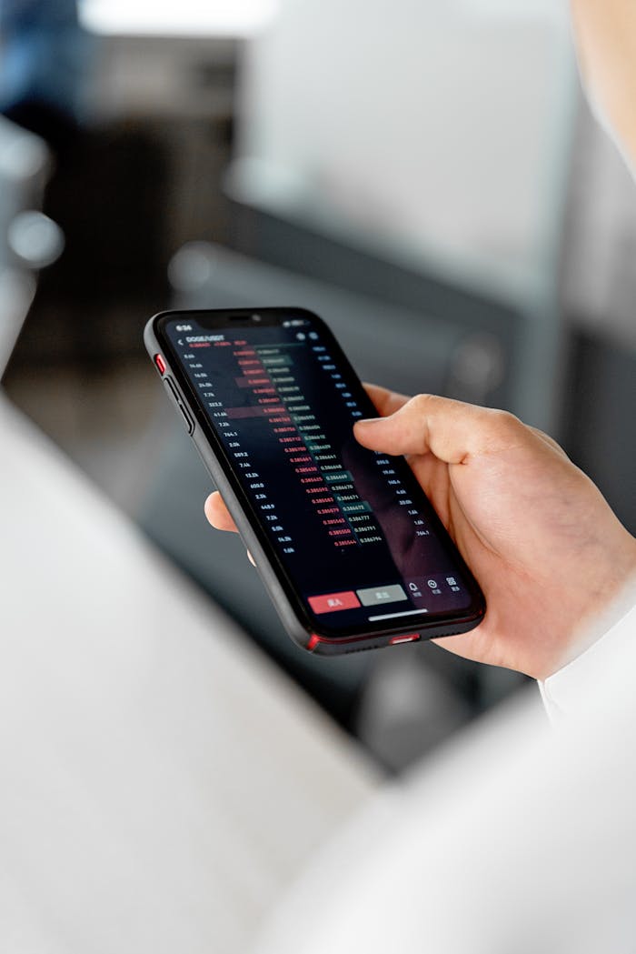 A close-up of a hand holding a smartphone displaying stock market data indoors.